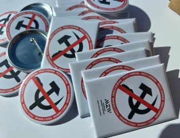 Zestaw białych magnesów prostokątnych i okrągłych przypinek z przekreślonym symbolem sierpa i młota oraz napisem Precz z Komuną, logo Muzeum Zimnej Wojny.