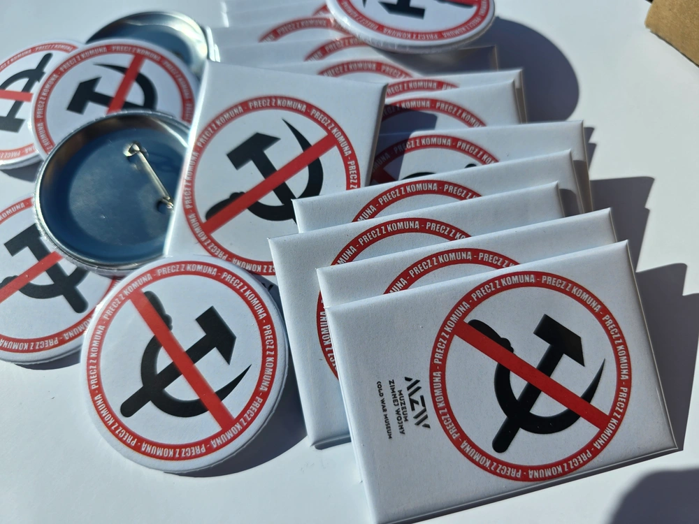 Zestaw białych magnesów prostokątnych i okrągłych przypinek z przekreślonym symbolem sierpa i młota oraz napisem Precz z Komuną, logo Muzeum Zimnej Wojny.